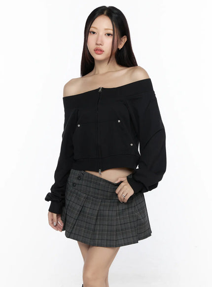 Off-Shoulder Zip-Up Cardigan CL527 Black front shot on model paired with dark plaid mini skirt, wide off-shoulder neckline, center front zip closure and snap button details