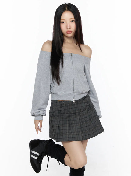 Off-Shoulder Zip-Up Cardigan CL527 Gray front shot on model with one leg raised, relaxed standing pose highlighting off-shoulder silhouette, zip front and snap details, plaid skirt styling