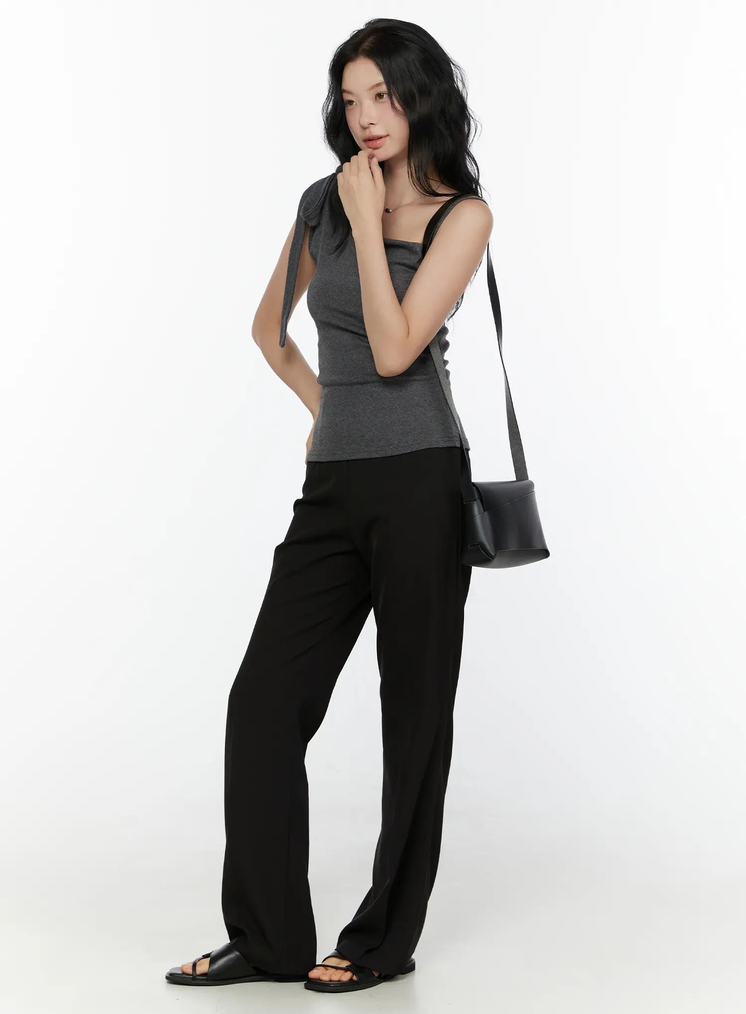 One-Shoulder Bow Top CL521 Dark gray full-body model side-angle shot hand to chin black cylinder bag styled with wide-leg trousers and flat sandals
