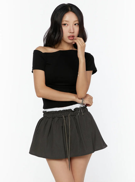 One-Shoulder Shirred Short Sleeve Top CU529 Black three-quarter front view on model with hand near chin showing asymmetric neckline and ruched crop fit