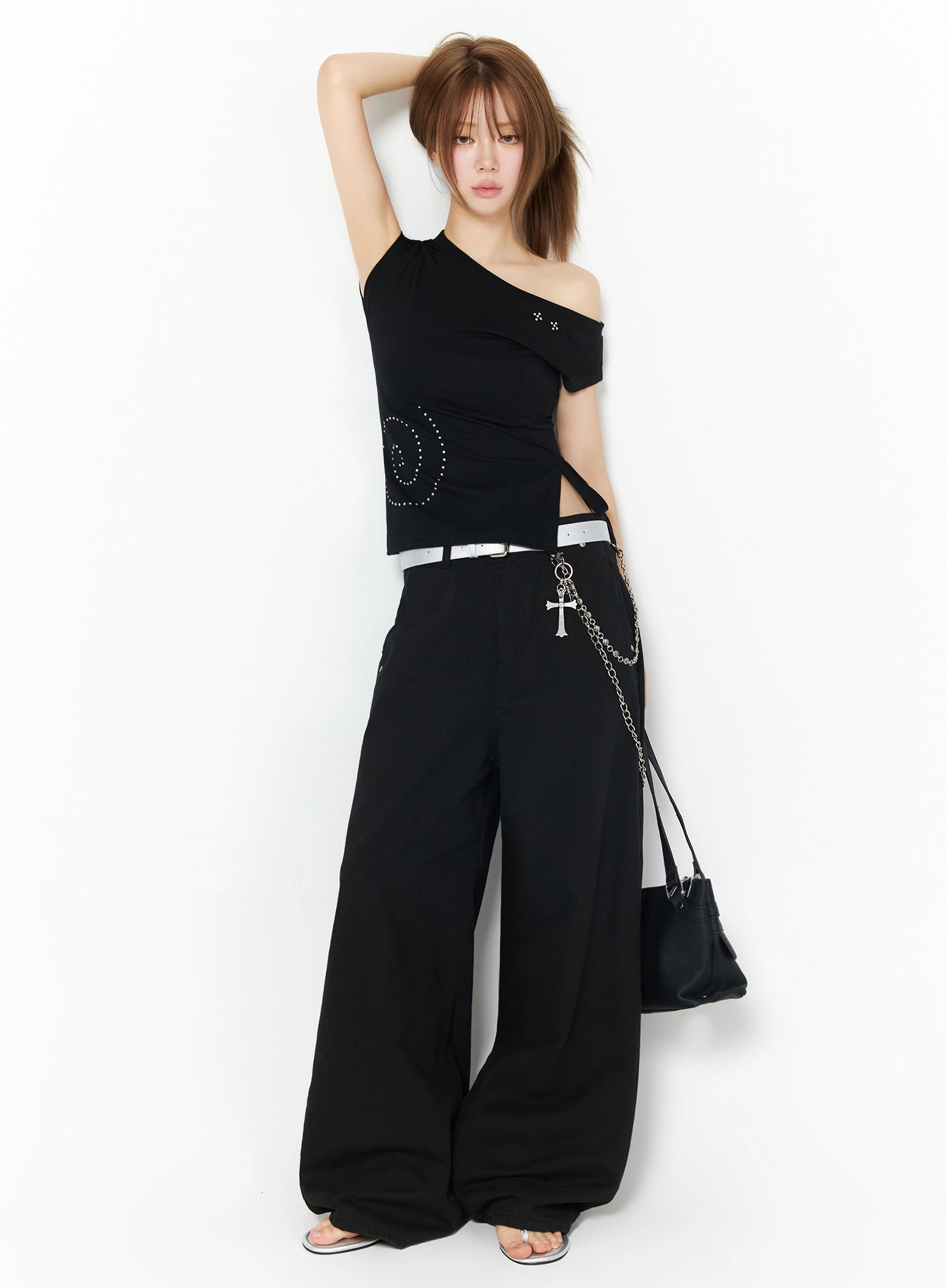 One-Shoulder Spiral Top IL502 Black full-length front shot on model with arm raised overhead, styled with white belt, chain accessory, wide-leg pants, and black bag