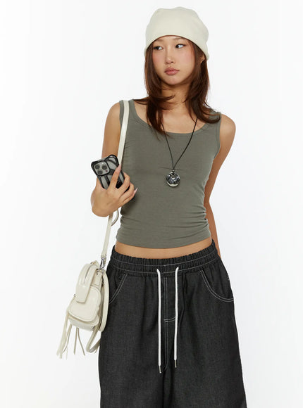 Open-Back Tank Top CL515 dark green three-quarter front shot on model with beanie and necklace, holding phone, showing cropped fitted silhouette and scoop neck