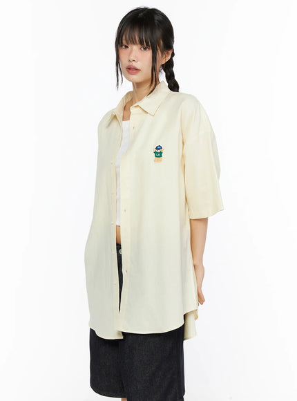 Oversized Button-Up Shirt CU530 Light yellow side shot on model showing open-front silhouette bear embroidery and relaxed elongated curved hem
