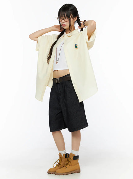 Oversized Button-Up Shirt CU530 Light yellow three-quarter side front shot on model hands raised to hair showing LA bear embroidery and relaxed long hem
