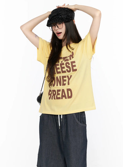 LEWKIN Oversized Graphic Tee CL522 Yellow front view on model wearing cap and glasses with arms raised overhead styled with wide-leg denim