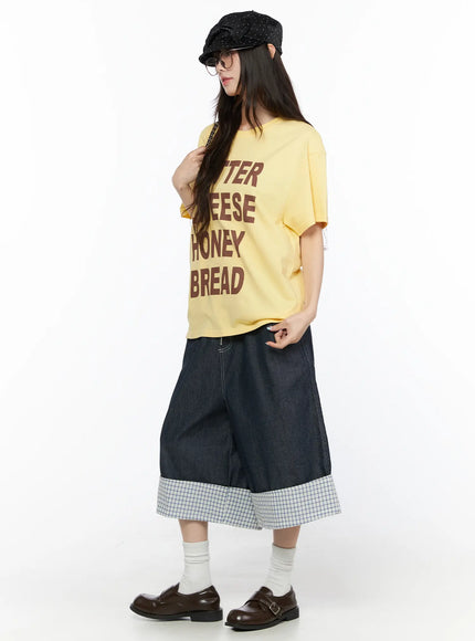 Oversized Graphic Tee CL522 Yellow three-quarter front view on model with cap and glasses hand touching shoulder styled with denim culottes