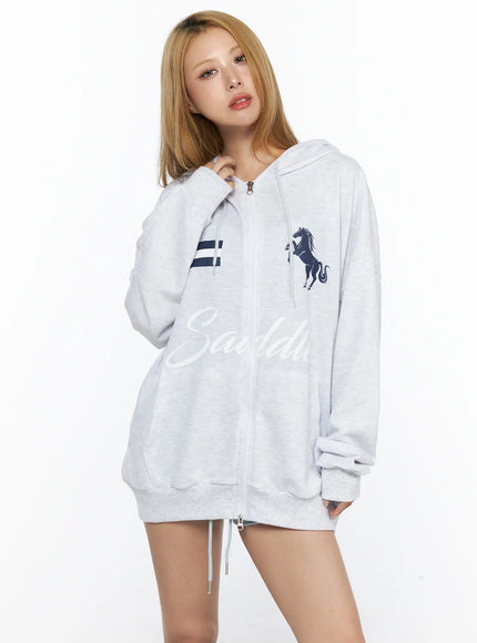 Oversized Graphic Zip-Up Hoodie CL528 Light Gray three-quarter front shot on model showing full-length zip placket navy horse graphic Saddle script print and drawstring hem