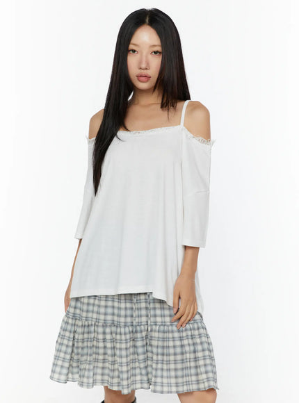Oversized Lace-Detail Off-Shoulder Tee CU529 White three-quarter front shot on model showing lace trim neckline off-shoulder silhouette and asymmetric hem with plaid skirt