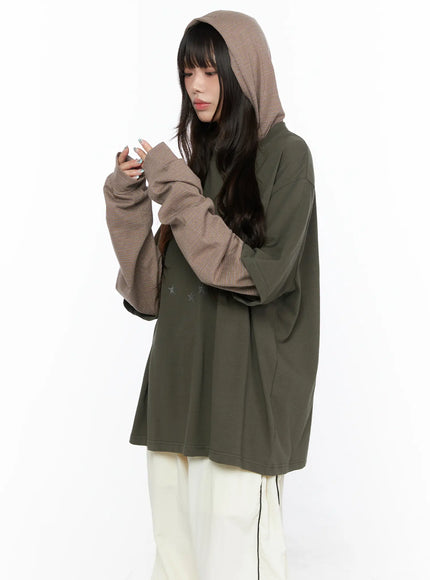 Oversized Layered Tee Striped Hoodie CL523 Dark green three-quarter model shot with brown striped hood up model looking down at hands showing layered sleeve detail