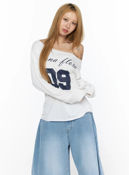 Oversized Off-Shoulder Graphic Long Sleeve Top CL528 White arms-crossed half-body front model shot highlighting off-shoulder neckline and navy 09 graphic print detail