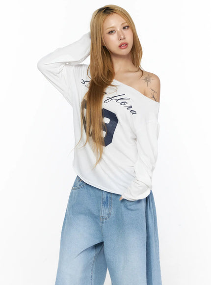 Oversized Off-Shoulder Graphic Long Sleeve Top CL528 White front model half-body shot hand in hair, off-shoulder neckline with Luna Flora script and partial 09 print visible