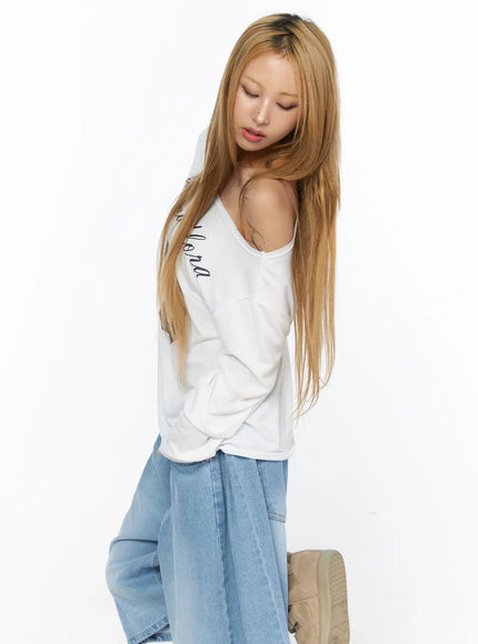 Oversized Off-Shoulder Graphic Long Sleeve Top CL528 White side model shot eyes-down showing off-shoulder drape, long sleeve silhouette, and relaxed fit with denim