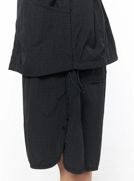 Oversized Plaid Windbreaker CU523 Black detail close-up shot showing grid-check nylon texture drawstring hood zip placket and short sleeves with teal layering top visible