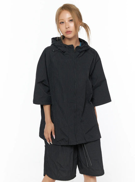 Oversized Plaid Windbreaker CU523 Black front close-up shot model wearing zip-up hooded windbreaker zipped closed showing grid-check nylon texture drawstring hood and raglan short sleeves