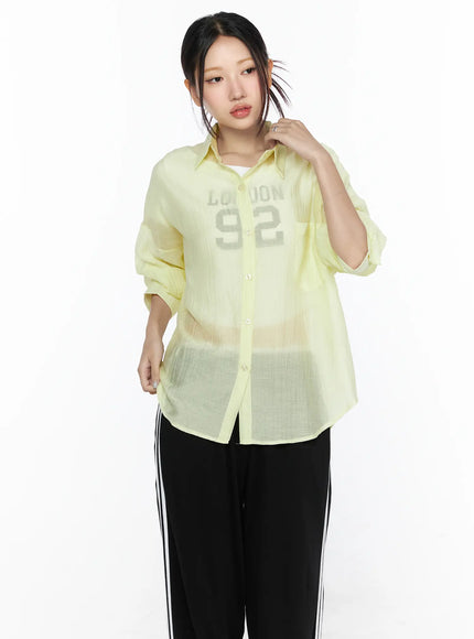 Oversized Sheer Shirt CL524 Yellow front model shot, hand raised to collar, relaxed fit with rolled sleeves, sheer crinkle fabric, paired with stripe trousers