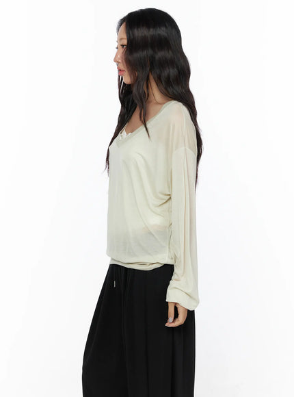 Oversized Summer Sheer V-Neck Long Sleeve Top CL513 Beige side model shot showing sheer long sleeve drape V-neck profile and ribbed waistband paired with black pants