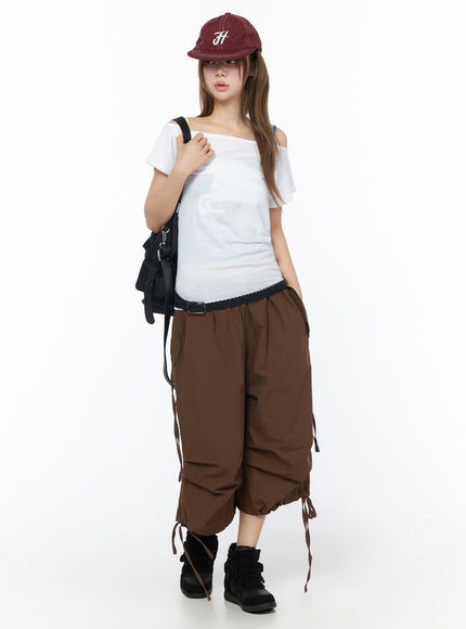 Parachute Cargo Shorts IU525 Brown full-body front on model styled with white off-shoulder tee, cap, black backpack, and black sneakers