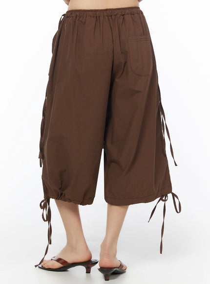 Parachute Cargo Shorts IU525 Brown back close-up on model showing back patch pocket, ribbon side ties, gathered balloon hem, and thong sandals
