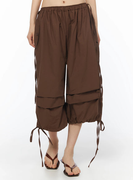 Parachute Cargo Shorts IU525 Brown front close-up on model showing elastic gathered waistband, side button pocket, and layered tiered hem with ribbon ties
