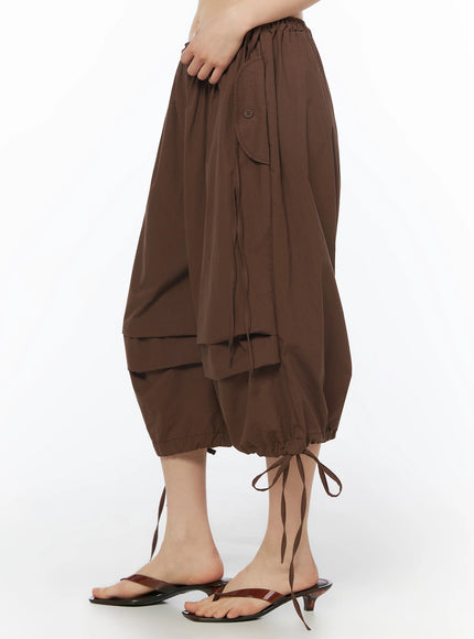 Parachute Cargo Shorts IU525 Brown side close-up on model showing hand at waist, curved patch pocket, button detail, drawstring, and balloon hem with tie