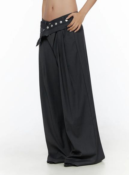 Pintuck Belted Wide Slacks CL510 dark gray side close-up on model, low-rise crossover waistband with silver studs, wide-leg fluid fabric, hand on hip