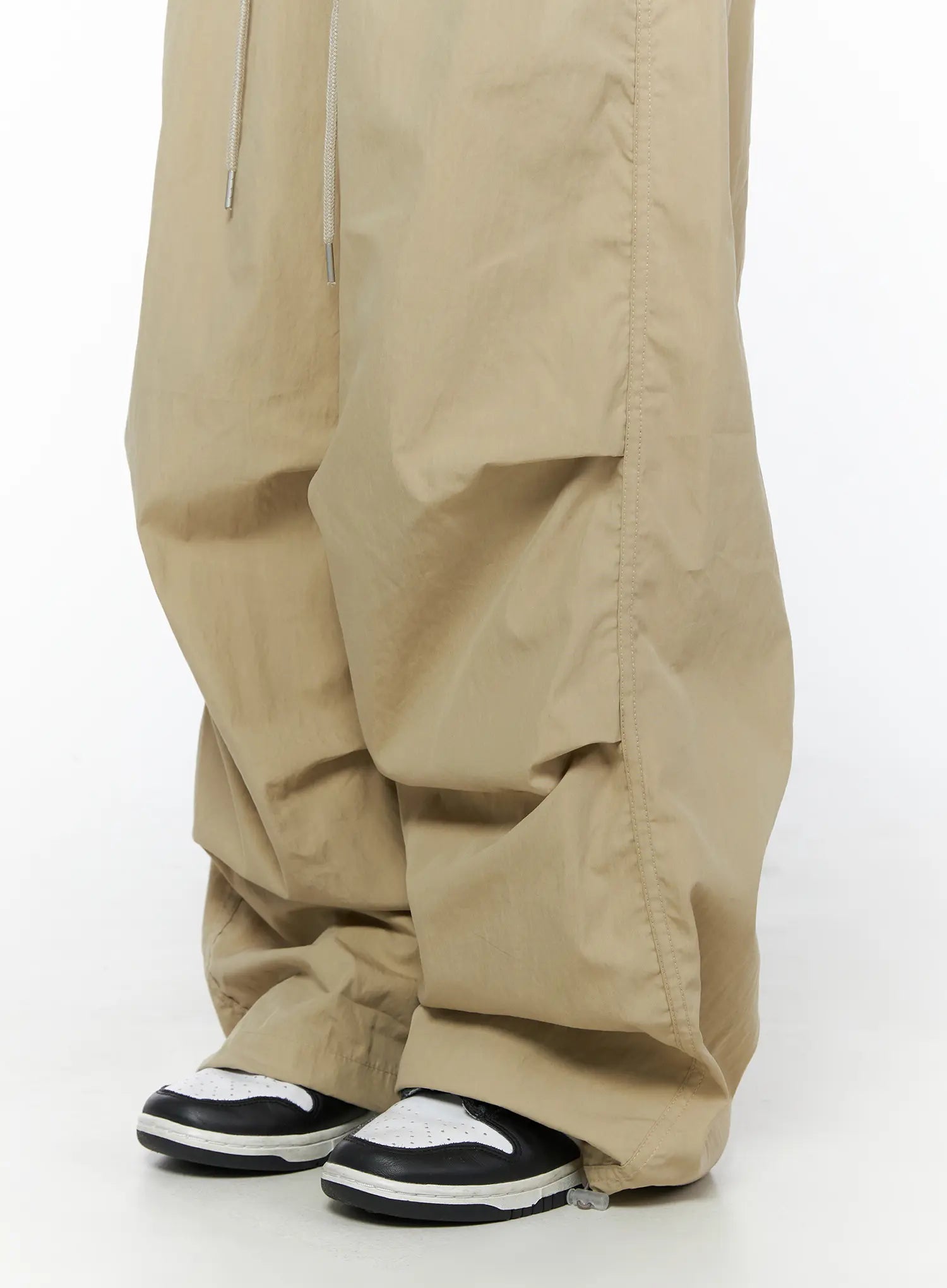 Pintuck Pocket Parachute Pants CU524 Beige close-up detail shot of lower leg showing voluminous gathered nylon fabric bunching over sneakers at hem