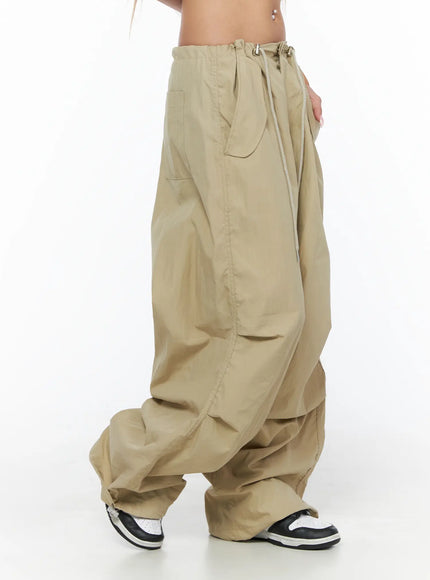 Pintuck Pocket Parachute Pants CU524 Beige side shot on model showing drawstring waist side pocket detail and voluminous wide-leg nylon fabric