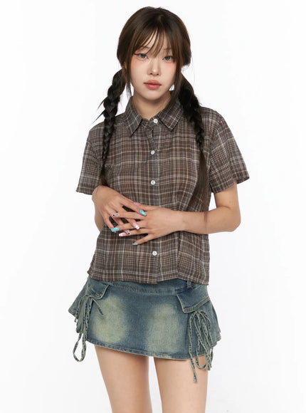 Plaid Crop Short Sleeve Shirt CL514 Brown half-body front shot on model with hands clasped showing buttoned placket collar and cropped hem over denim mini skirt