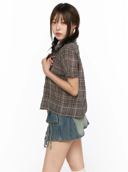 Plaid Crop Short Sleeve Shirt CL514 Brown side shot on model holding braid hand at chest showing cropped length and plaid weave detail with denim mini skirt