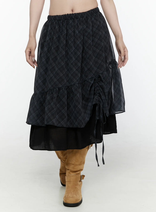 LEWKIN Plaid Layered Midi Skirt IL522 Black S/M front shot on model cropped view showing elastic waistband diagonal plaid sheer overlay ruched drawstring tie tiered ruffle hem with black underlayer styled with tan boots