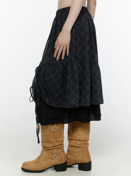 Plaid Layered Midi Skirt IL522 Black side shot on model cropped waist-down view showing ruched drawstring tie on outer layer tiered ruffle hem black underlayer sheer plaid fabric with tan boots