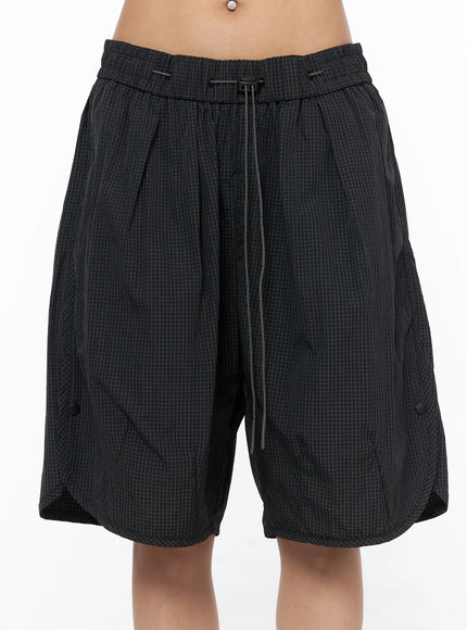 Plaid Nylon Shorts CU523 Black front close-up on model, grid-pattern nylon fabric with pleated front, elastic waistband and drawstring detail
