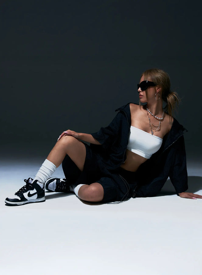 Plaid Nylon Shorts CU523 Black lifestyle shot, model seated on floor wearing black grid nylon shorts with open jacket, white crop top, sneakers