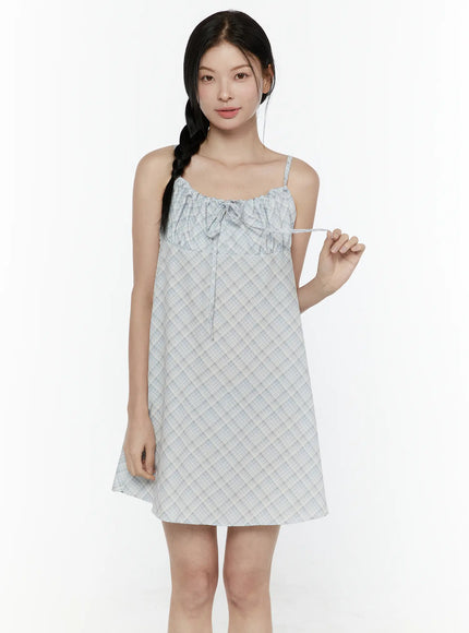 Plaid Shirred Cami Mini Dress IL506 Light blue front model shot model holding tie drawstring showing adjustable ruched neckline and A-line silhouette