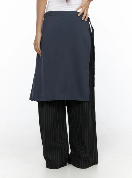 Pleated Midi Wrap Skirt CL513 navy blue front detail shot model hand on hip showing flat smooth outer skirt panel layered over black pinstripe wide-leg trousers without belt