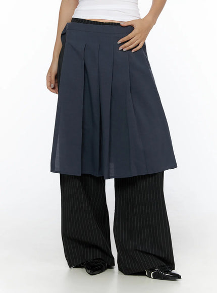 Pleated Midi Wrap Skirt CL513 navy blue front close-up shot model hand on skirt showing deep box pleats flared hem and layered contrast pinstripe trouser leg below