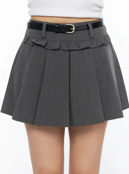 Pleated Mini Skirt CL517 Gray close-up front detail shot on model showing ruffle trim, black leather buckle belt, woven fabric texture and deep knife pleats