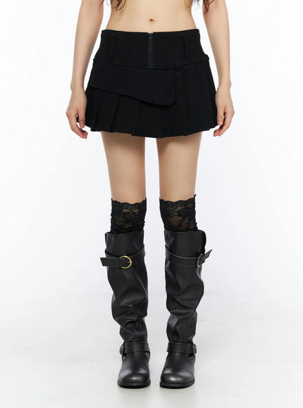 Pleated Mini Skirt CU530 Black front view on model with lace socks and black knee-high boots, arms relaxed showing layered flap and zipper