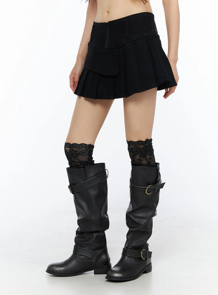 Pleated Mini Skirt CU530 Black side view on model with lace socks and black leather boots, showing pleated skirt silhouette and flap detail