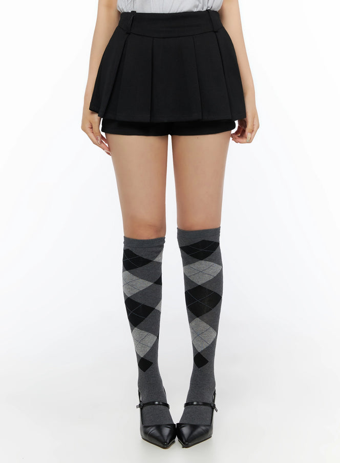 LEWKIN Pleated Mini Skirt IL523 Black front view on model wearing argyle knee-high socks and black heels, pleated skort silhouette, size S