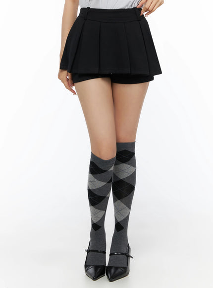 Pleated Mini Skirt IL523 Black front close-up on model from waist to toe showing box pleats, inner shorts, and grey argyle knee-high socks