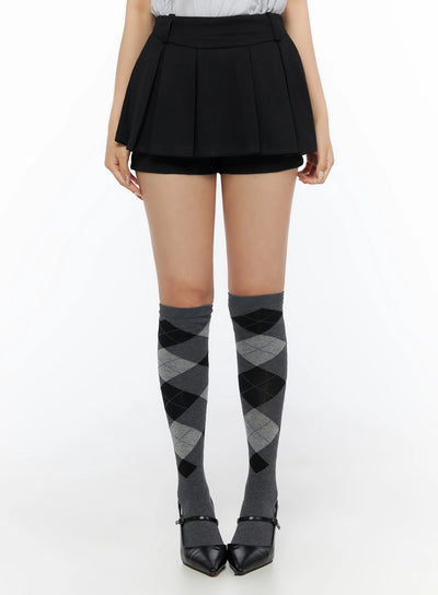 LEWKIN Pleated Mini Skirt IL523 Black front view on model wearing argyle knee-high socks and black heels, pleated skort silhouette, size S