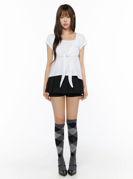 Pleated Mini Skirt IL523 Black full-body front shot on model with white tie-front top, arms at sides, argyle over-the-knee socks, black heels