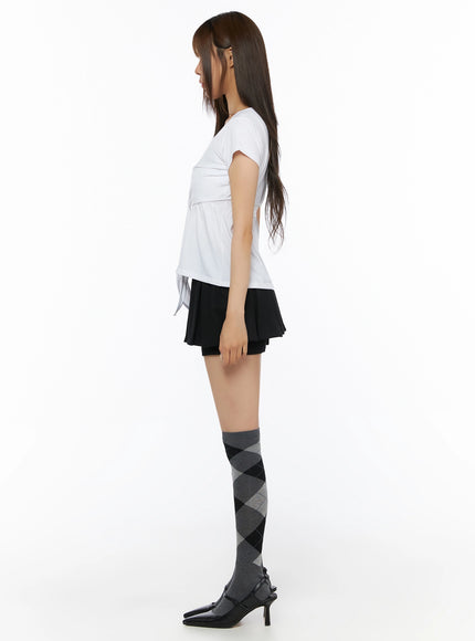 Pleated Mini Skirt IL523 Black full-body side shot on model showing silhouette of pleated skirt overlay and tie-front white top, argyle socks