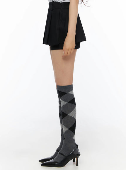 Pleated Mini Skirt IL523 Black side close-up on model from hip to toe showing pleated skirt silhouette and grey argyle over-the-knee sock