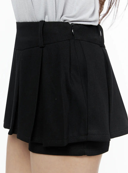 Pleated Mini Skirt IL523 Black close-up side detail on model showing pleated panel, side zipper, high waistband, and inner shorts layer