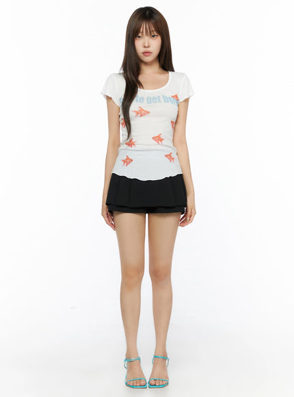 Pleated Skort IL515 Black full-body front shot on model with straight hair, styled with white goldfish print tee and teal strappy sandals, standing straight