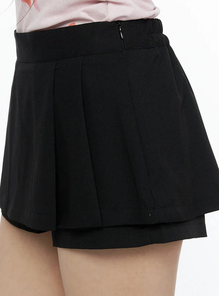 Pleated Skort IL515 Black close-up side detail shot on model showing side zipper closure, pleated panel seams, and double-layer hem construction