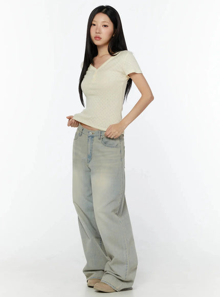 Pointelle Slim Henley V-Neck Tee IU524 Light beige diagonal side shot model holding hem showing cropped length and slim pointelle fit paired with wide-leg jeans