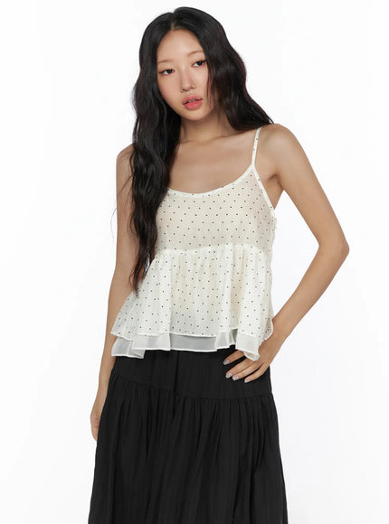 Polka Dot Frill Sleeveless Top CL510 Ivory three-quarter front shot on model with hand on hip showing black polka dot pattern on sheer tiered ruffle top